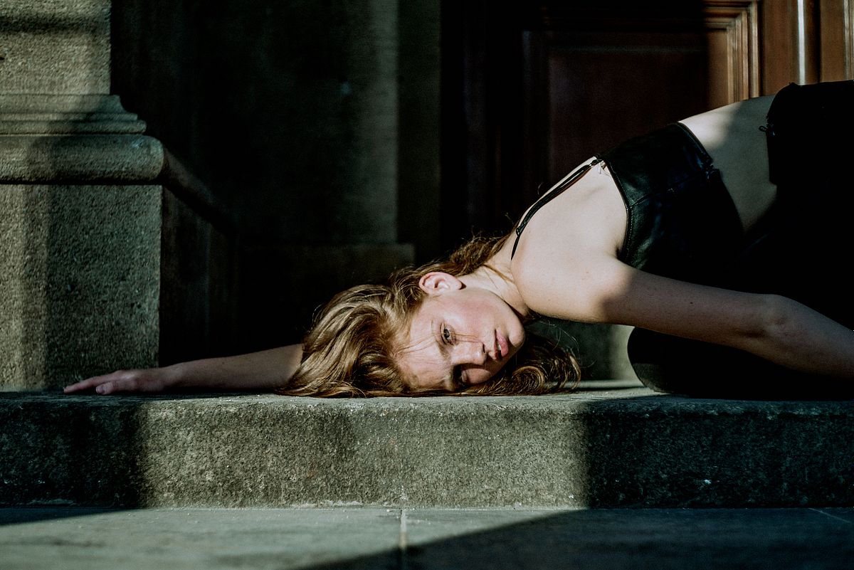 Cinematic editorial portrait of a young woman lying on stone steps in soft natural light, Pure Models Prague, by Gabriel Matula.