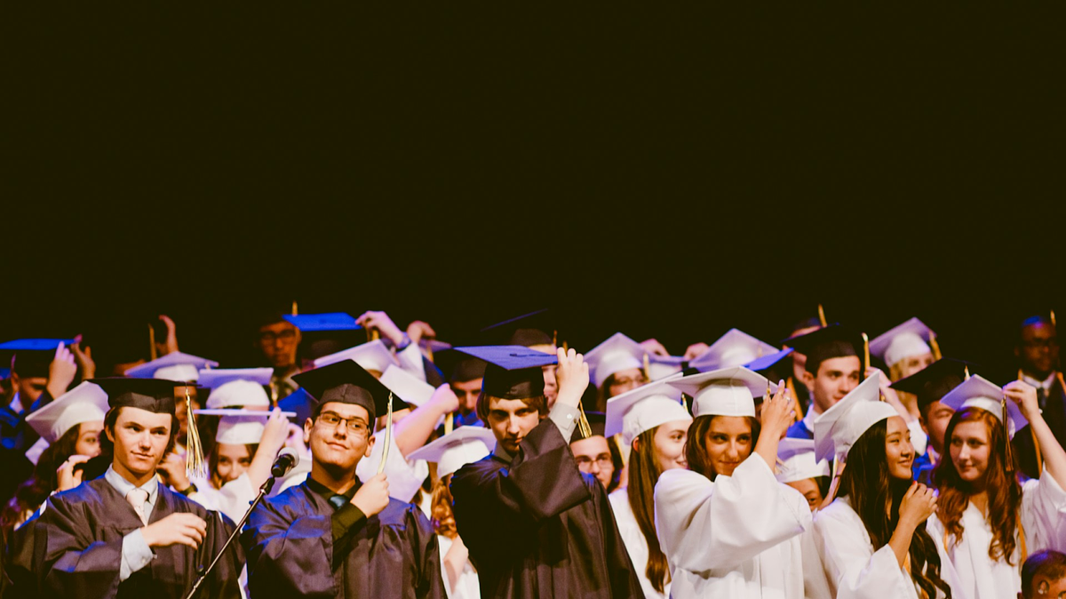 Hombres y mujeres con vestidos de graduación en blanco y negro y birrete dentro del edificio