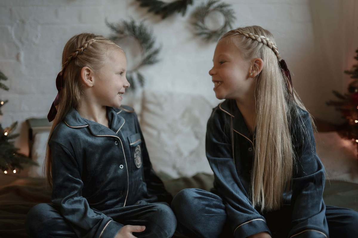 Two girls with braided hair facing each other in satin pyjamas, children's lifestyle photography