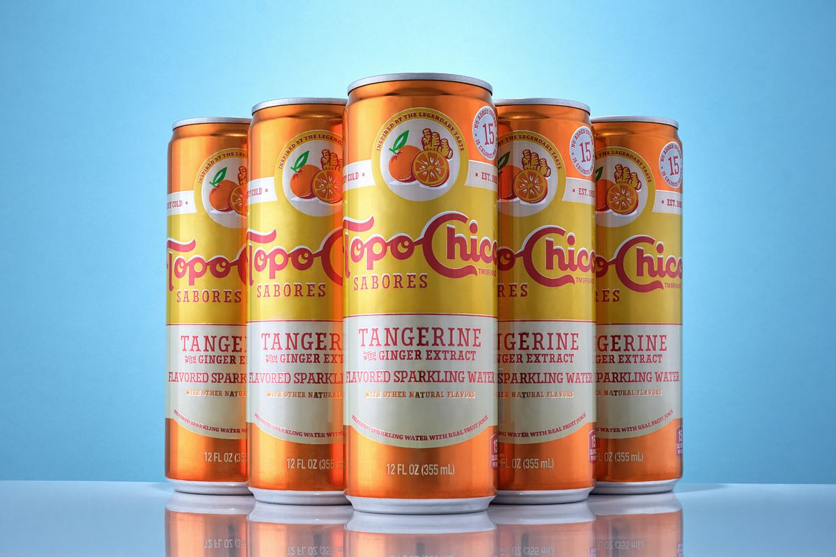 Five orange, yellow and white beverage cans on a light blue background.
