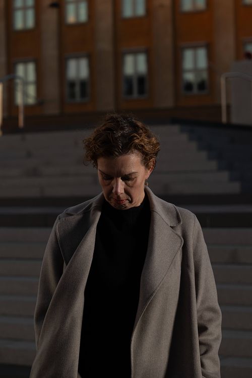 Candid porträtt av kvinna i kappa som blickar ned, fotograferad i stadsmiljö vid trappa, personal branding i Stockholm.