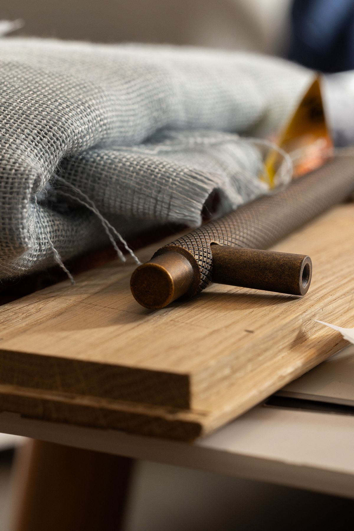 N&auml;rbild av ett m&ouml;rkt metallbeslag p&aring; tr&auml;prov med tygprover i bakgrunden, som del av inredningsdesign och materialval.