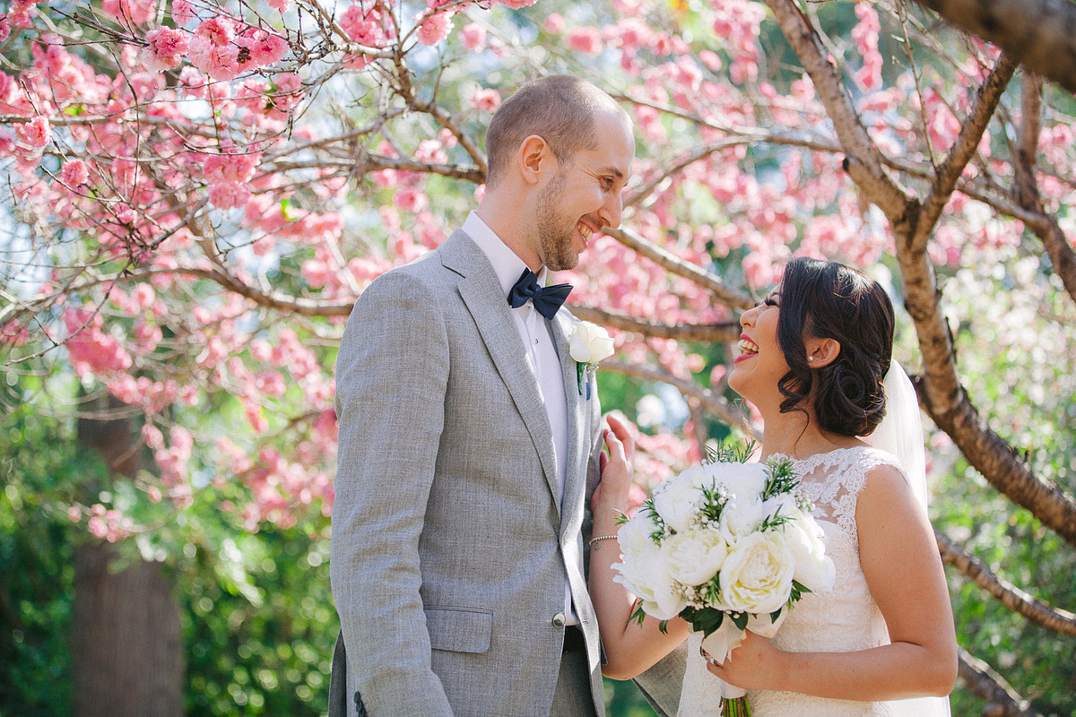 Candid moment captured in wedding photography as the couple shares a laugh under cherry blossom tree at Japanese Garden