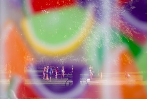 Families hula hooping in a serene park, with reflections of colorful candy slices from a nearby candy shop