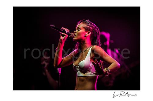 Horizontal color image of Rihanna singing into a microphone in side profile under vivid magenta stage lighting