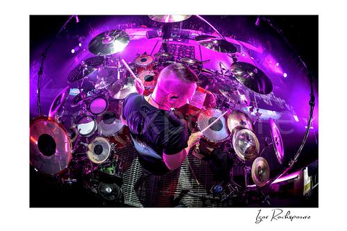 Horizontal color image of Korn drummer Ray Luzier seen from above at the drums under vivid purple stage lighting