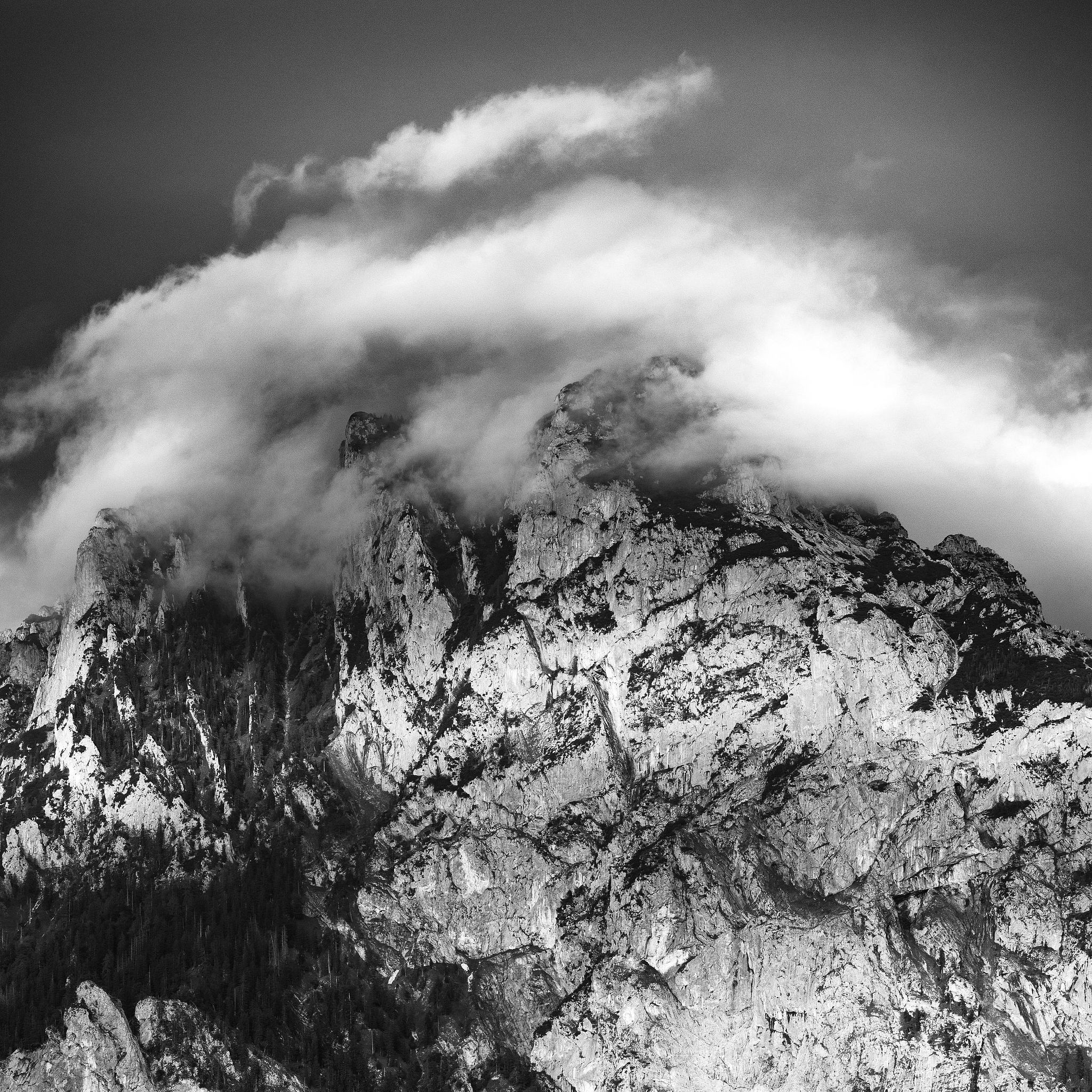 Black and white mountain ridge emerging through dense clouds – fine art photography by Florent Baudy