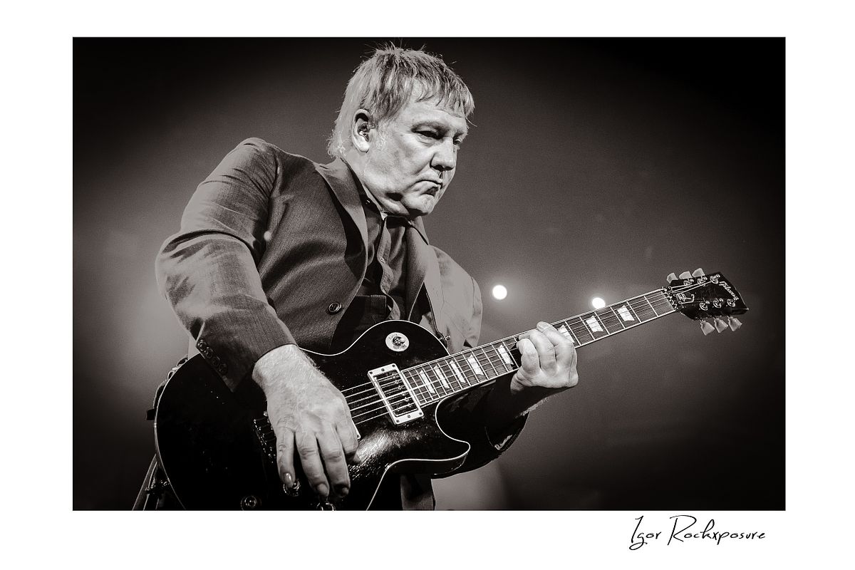 Horizontal concert photography of Alex Lifeson playing electric guitar in black and white photography under stage lighting