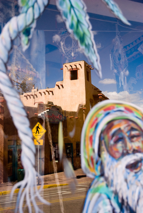Painted face in store window juxtaposed against adobe building on Manitou Springs main street in background