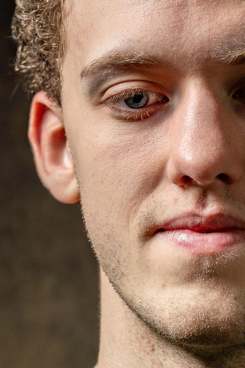 Halvt ansikte av ung man i studioljus, skarp hudstruktur och blick