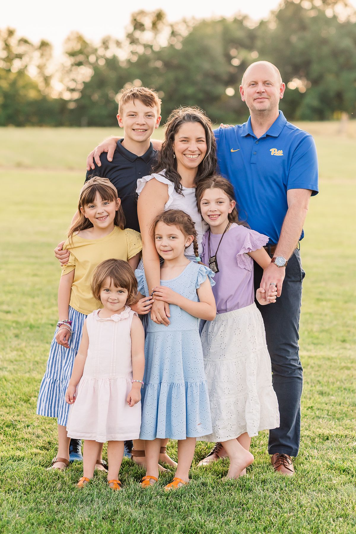 Family of 7 in open field in sunset light, smiling and huddled together at Cranberry Township Community Park