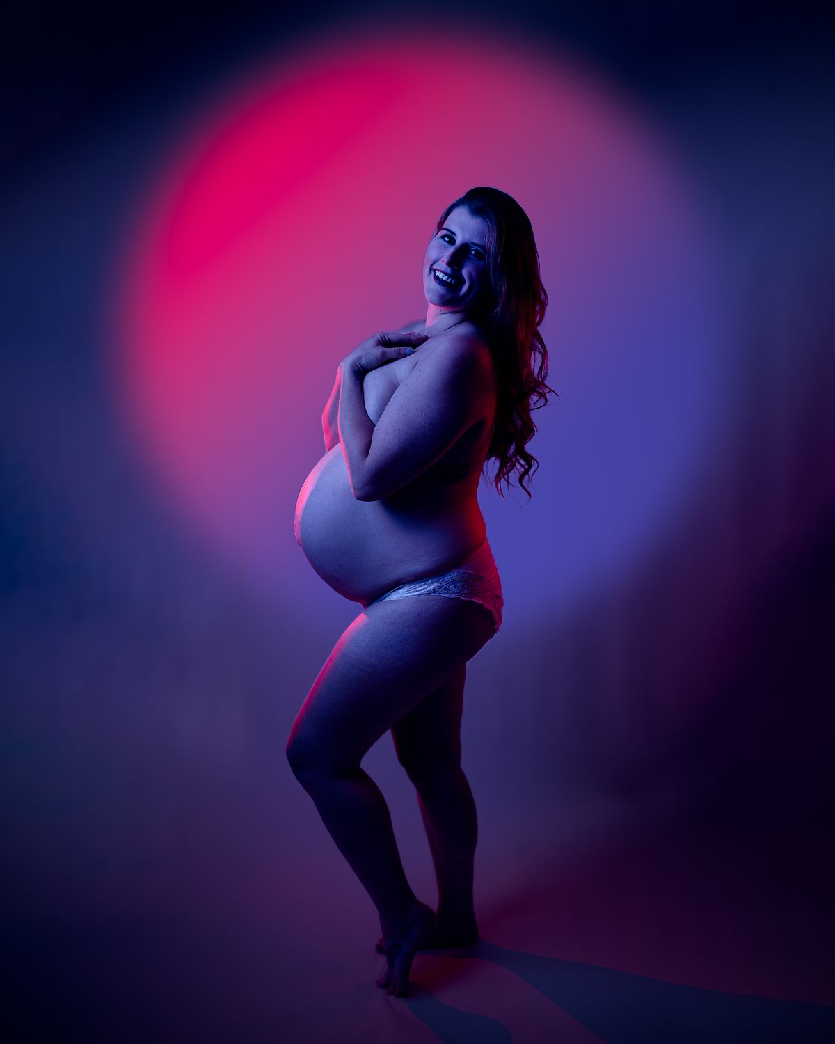 Portrait of an expectant mother lit with neon light in front of a glowing pink circle.