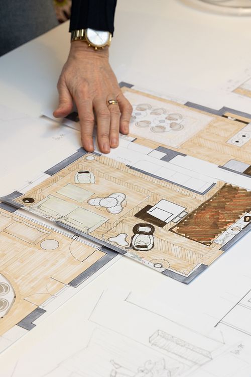 Hand som pekar på en färglagd inredningsplan med möblering och rumslayout på bord.