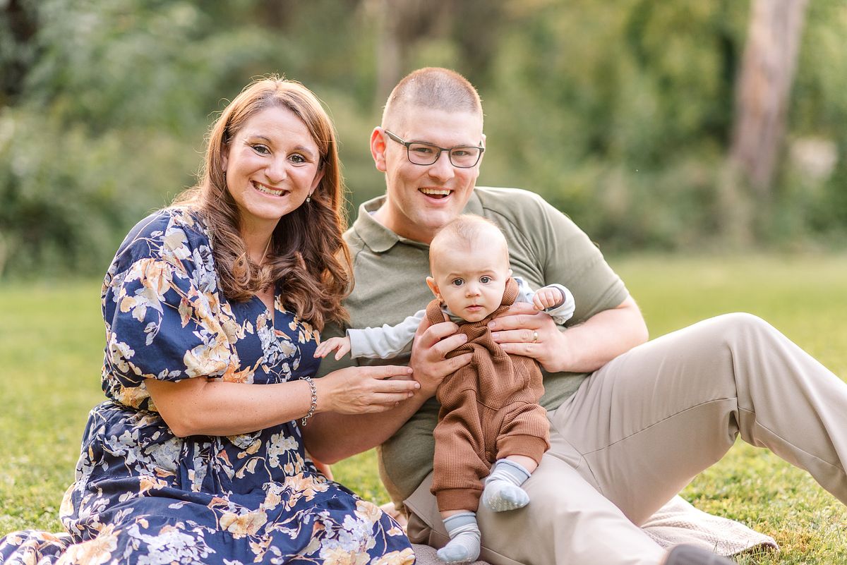 New parents sitting on the ground in a park, holding their baby
