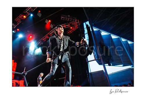 Horizontal color image of Klaus Meine of Scorpions striding across the stage with microphone stand under red and blue concert lights