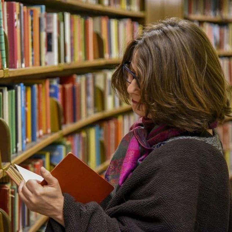 woman reading books in a library surrounded by shelves of books