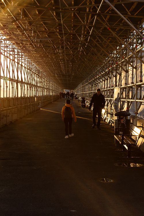 Industrial walkway at golden hour with people walking into the distance, photographed in Stockholm by Mats Karlsson.