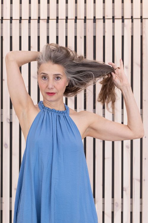 Nära porträtt för personal branding – person i blå klänning med lekfull gest framför träspaljé.