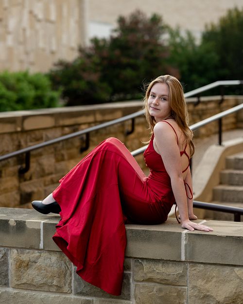 Portrait of a young woman in a red dress sitting on concrete steps.