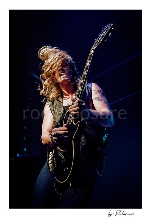 Vertical color image of Jared James Nichols playing guitar onstage with flying hair under blue concert light