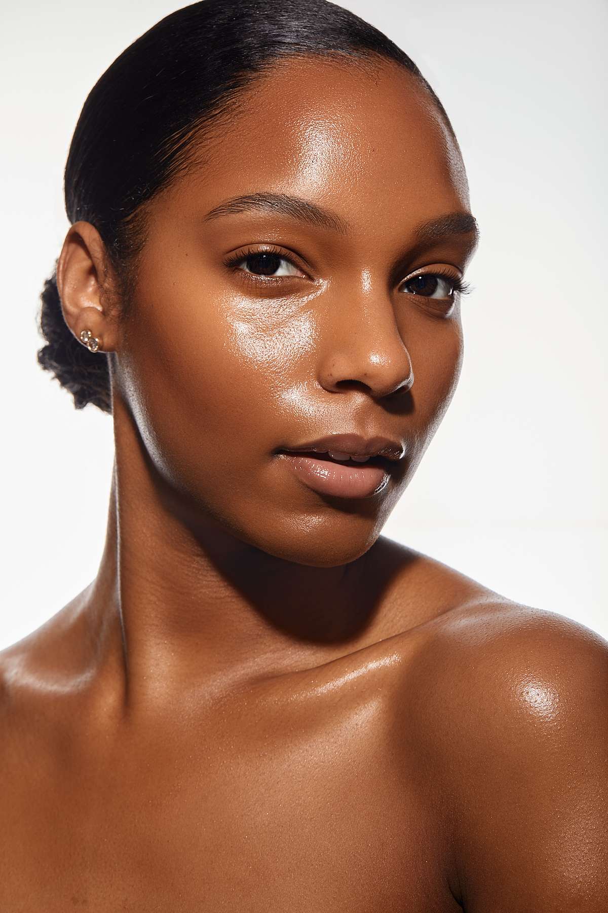 Close-up portrait of a woman with radiant, dewy dark skin and slicked-back hair.