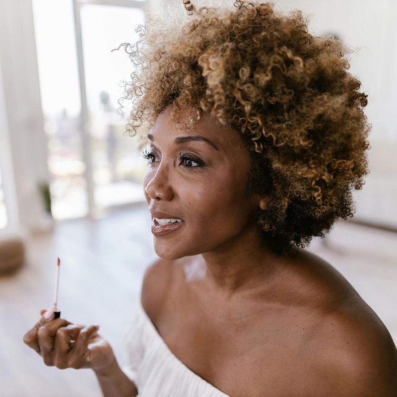 profile of a woman looking into mirror and applying makeup