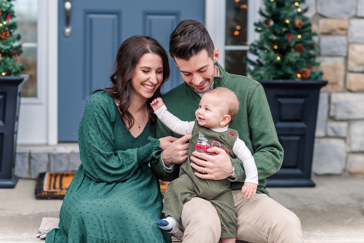 Husband and wife sitting on porch holding and looking at their baby who is playing with Cranberry Township, PA newborn photographer