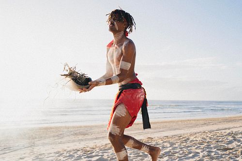 Queen's Baton Relay Australia, Indigenous Australian walks on a beach preparing a smoking ceremony