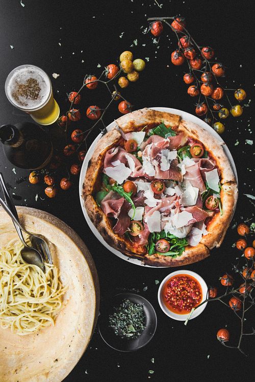 Pizza with tomato, fior di latte, prosciutto crudo and rocket on a black table with a Peroni