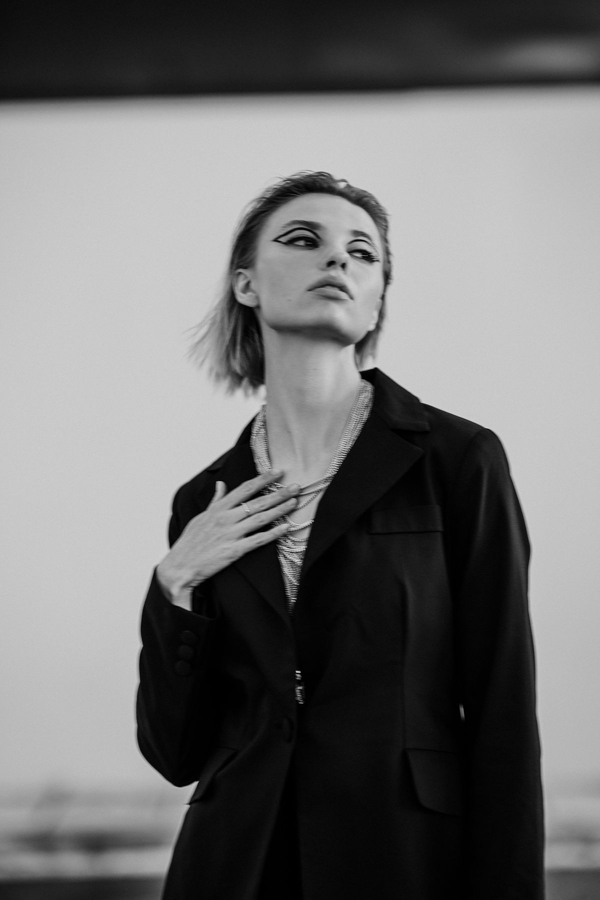 Black & white portrait of a female model in motion, wearing a black blazer and statement necklace. Photographed by Filianna Karamanli.