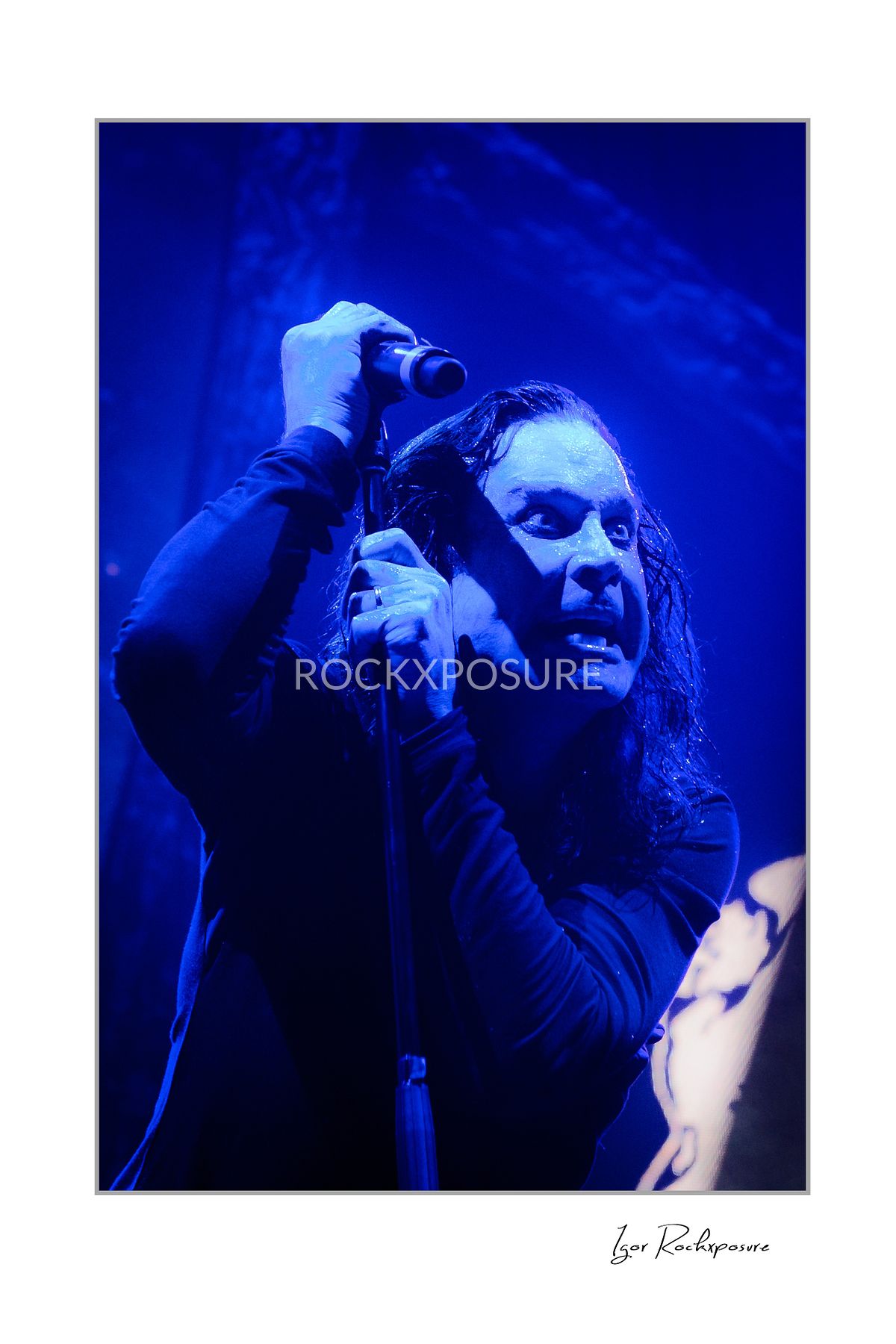 Ozzy Osbourne of Black Sabbath holding a microphone above his head during a live performance under deep blue concert lighting