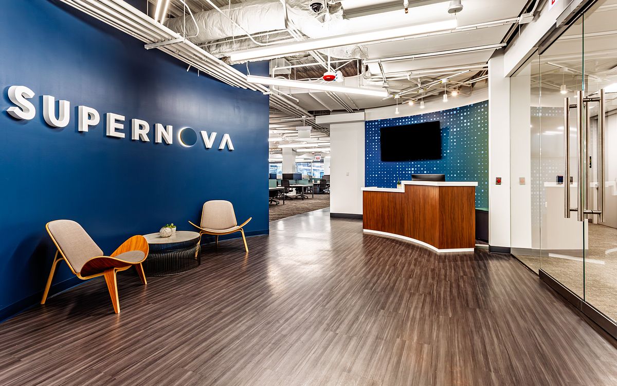 Modern corporate reception area for Supernova Technology in Chicago featuring a large blue brand wall, mid-century lounge chairs and a wood-slat front desk