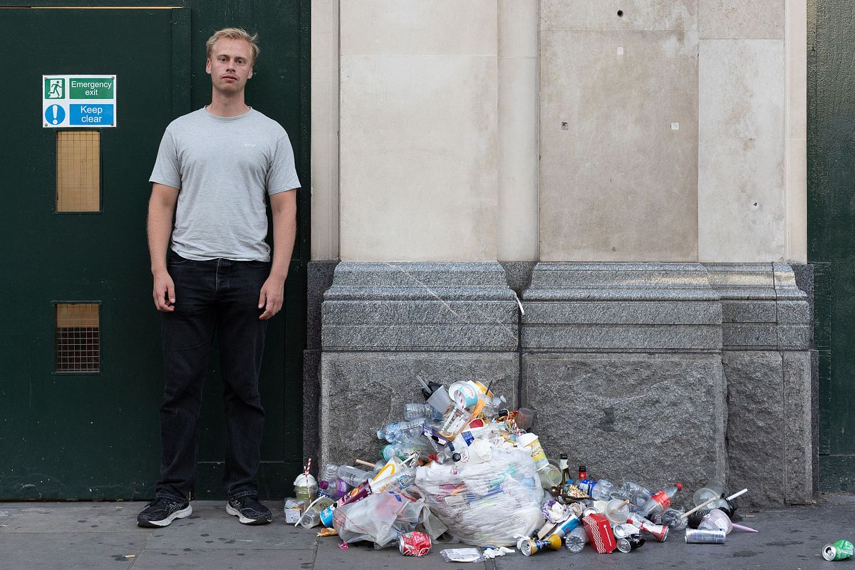 Man st&aring;r vid en v&auml;gg bredvid en h&ouml;g med skr&auml;p och pantflaskor, dokument&auml;rt portr&auml;tt i urban milj&ouml;.