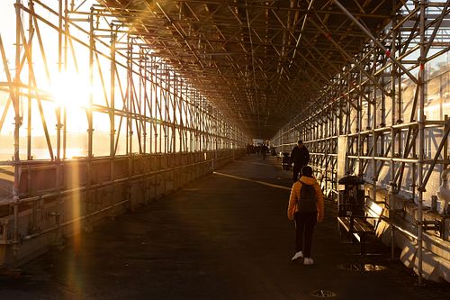 Lång gång under byggställning i motljus med solstrålar och människor som promenerar