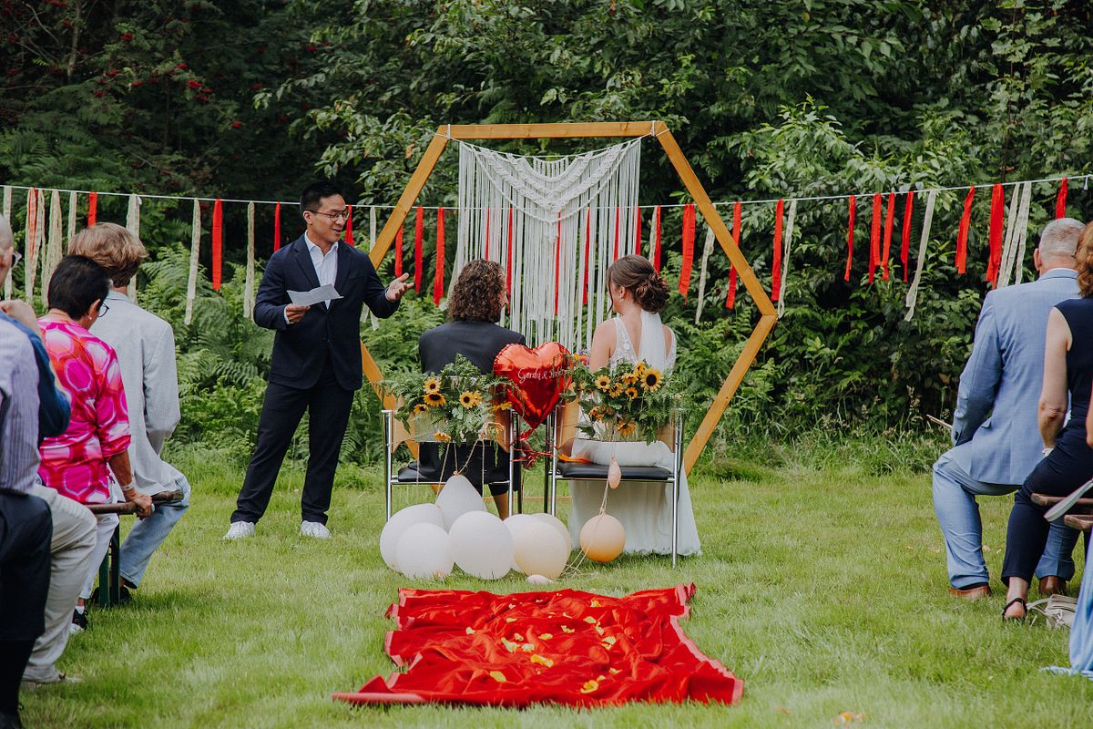Das Brautpaar steht von hinten zur Kamera blickend vor dem Traubogen bei ihrer Freien Trauung, emotionale Reportage in einer Outdoor-Location in NRW.