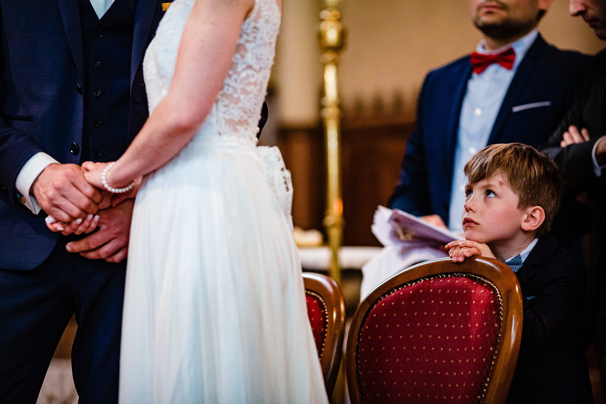 Enfant durant la c&eacute;r&eacute;monie religieuse qui regarde ses parents se tenir la main captur&eacute; par S&eacute;bastien CLAVEL photographe de Mariage &agrave; Lyon et Gen&egrave;ve
