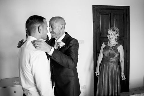 "la mamma dello sposo guarda lo sposo che si fa allacciare dal padre"