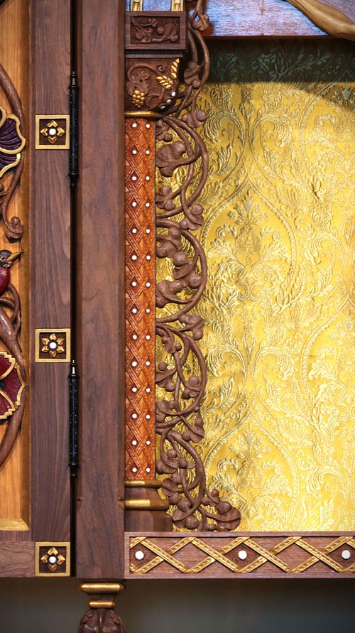 Close up of an ornately carved column with a Eucharistic capital and flowing vines that provide a frame for the Crucifix in the altarpiece.
