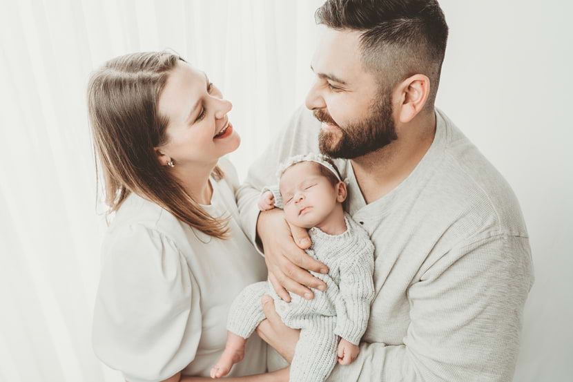 Happy family grinning to each other while holding their precious newborn in Cypress, TX