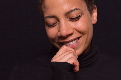 A headshot of a woman smiling, with a hand placed against her mouth, dressed in a black turtleneck.