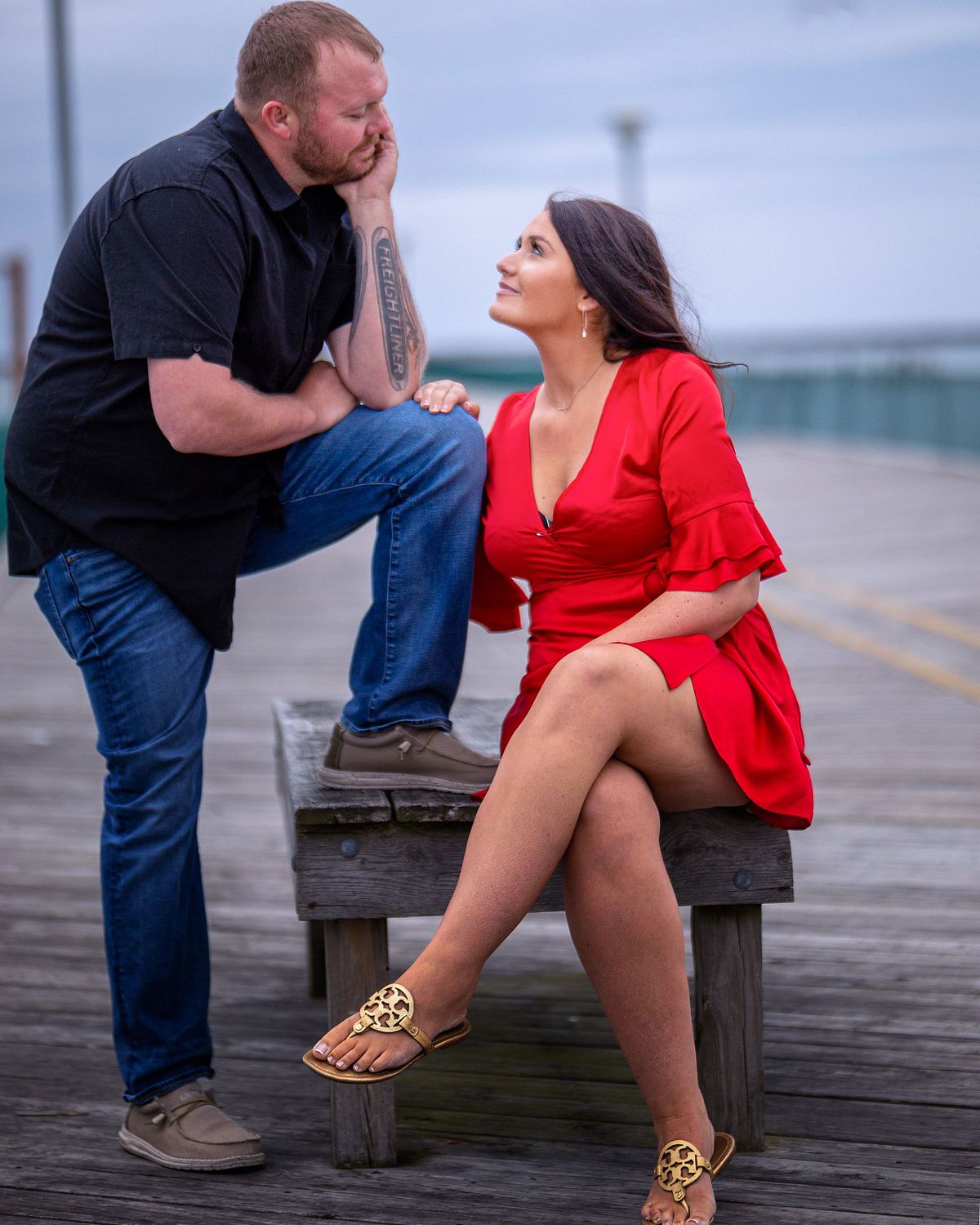 couple posing on the pier in cape henlopen for a romantic valentine proposal the woman is wearing a red dress in celebration of the event.