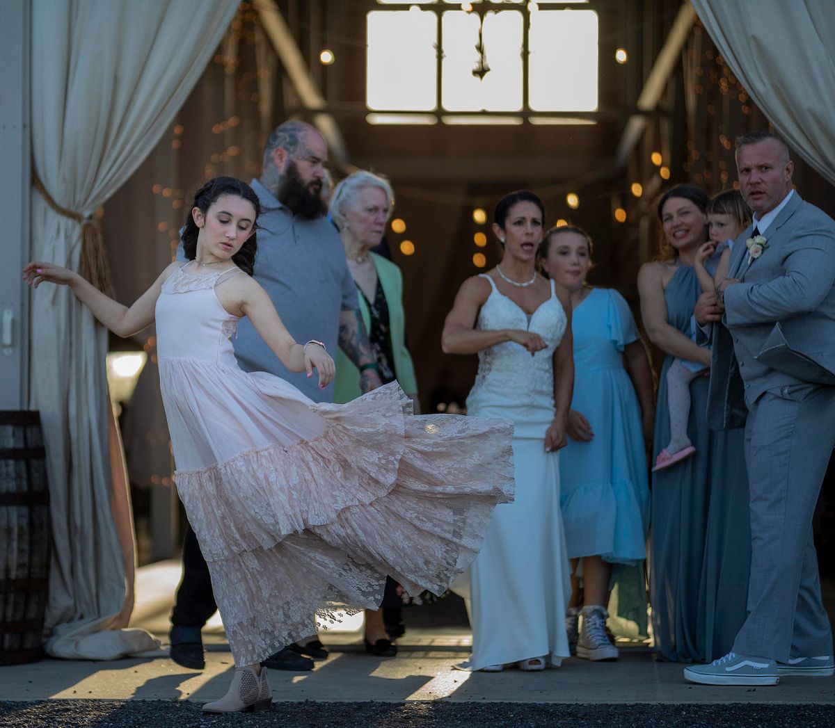 family photo in front of kylan barn, with the flower girl dancing in front of the wedding party