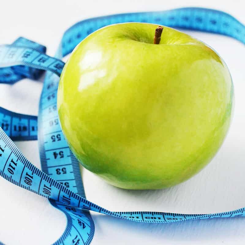 green apple surrounded by a blue tape measure for healthy weight loss