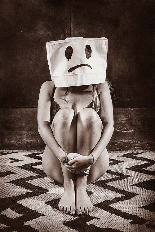 Femme assise au sol en lingerie avec un sac en papier sur la t&ecirc;te affichant un visage triste, illustrant l&rsquo;&eacute;puisement &eacute;motionnel et la solitude int&eacute;rieure malgr&eacute; une fa&ccedil;ade sociale