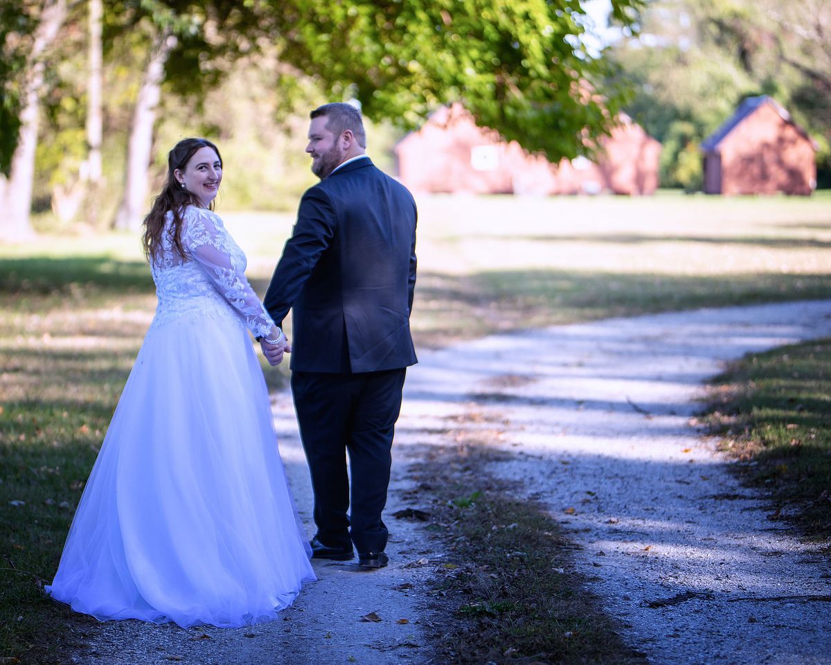 newly wed couple walking towards the remodeled out buildings at ross mansion, the bride is looking back at the photographer smiling