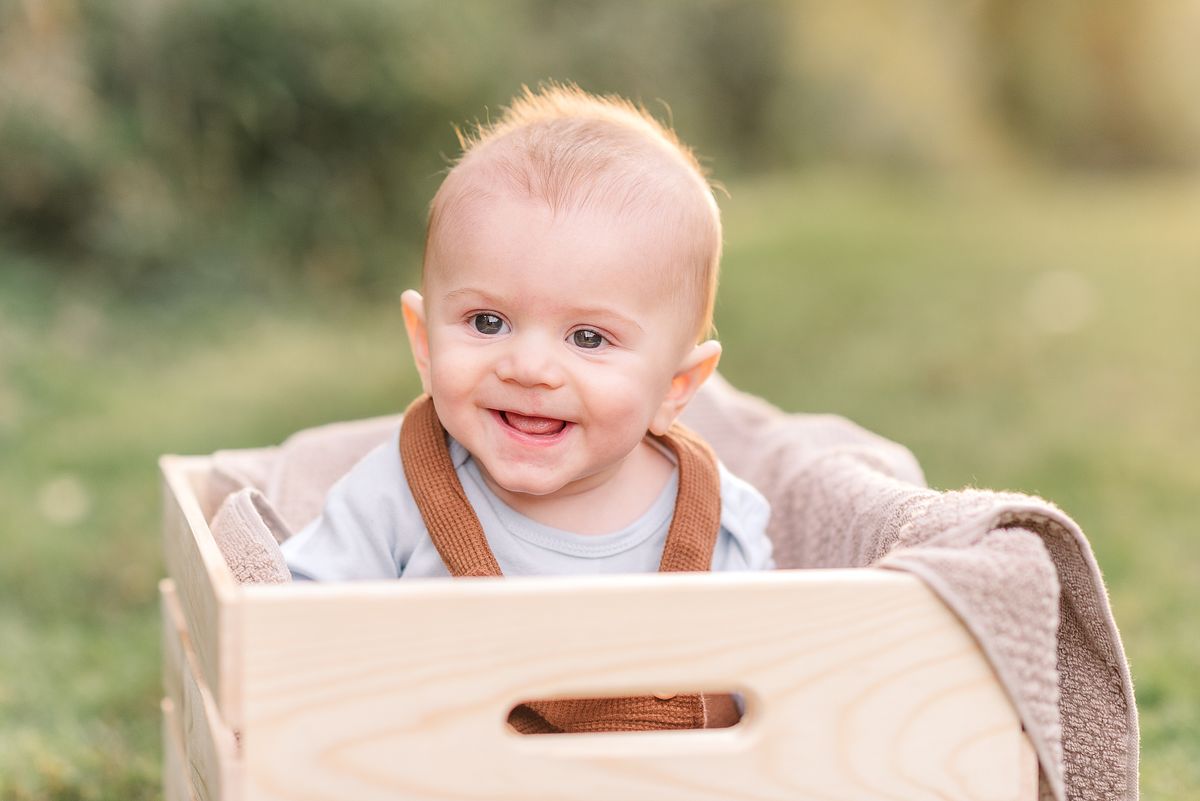 Baby smiling and sitting in a wooden crate at a park