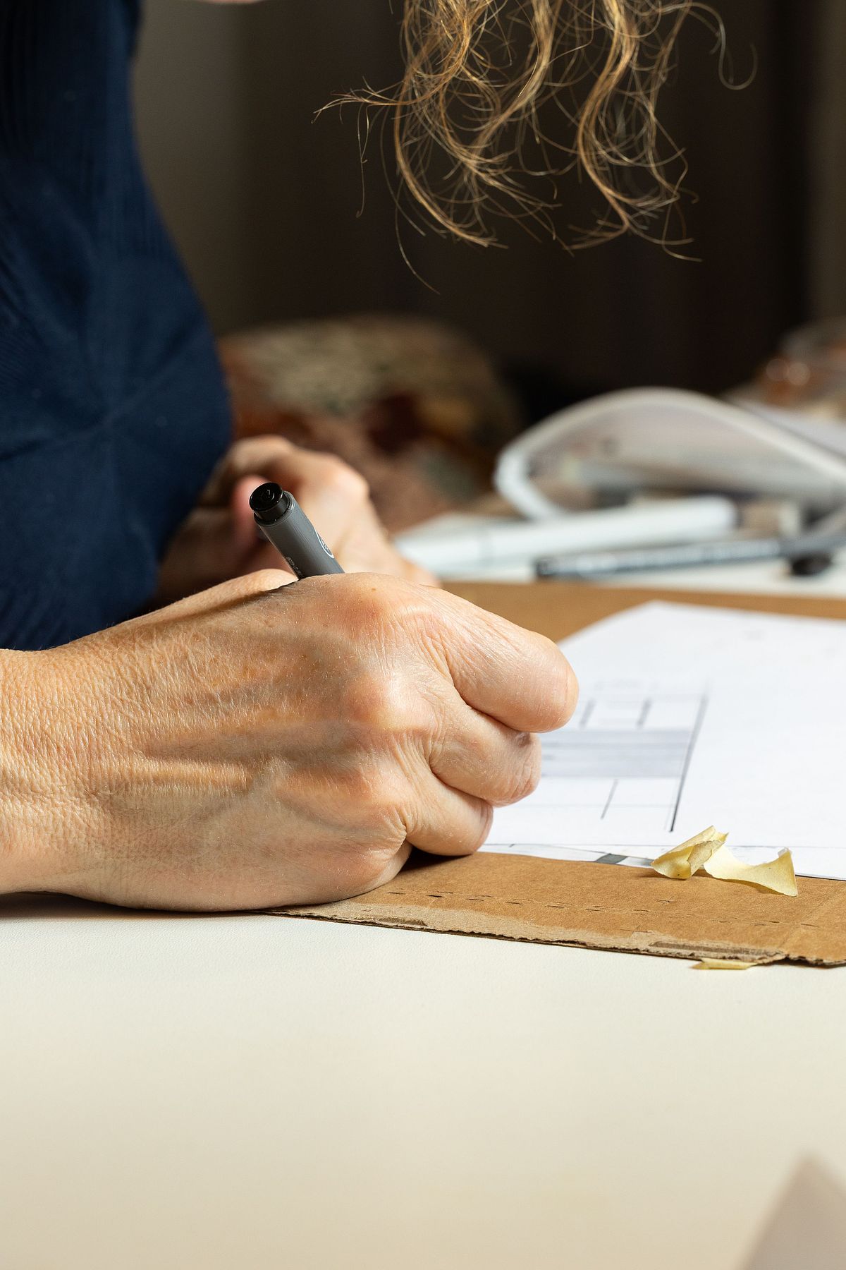 N&auml;rbild av hand som ritar med penna p&aring; papper vid bord &ndash; fokus p&aring; kreativ process.