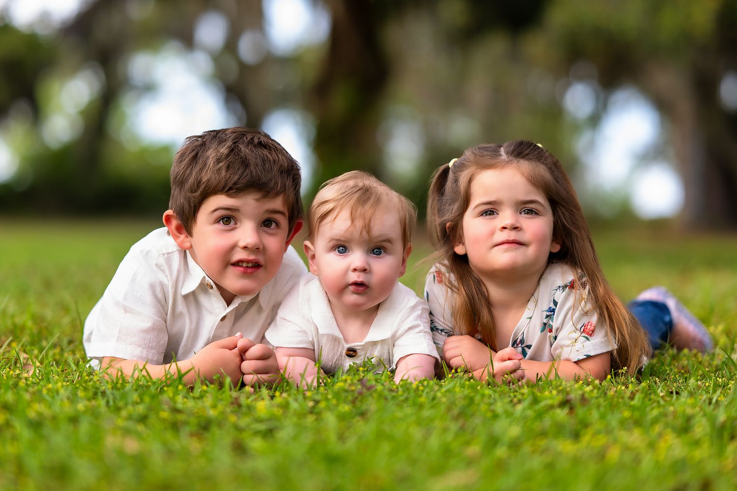 Three young children lying side by side and looking at the camera during a professional family photography session in Beaufort, South Carolina.