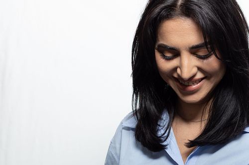 Studioporträtt av skådespelare med nedåtblick och naturligt leende, neutral bakgrund och mjukt ljus.