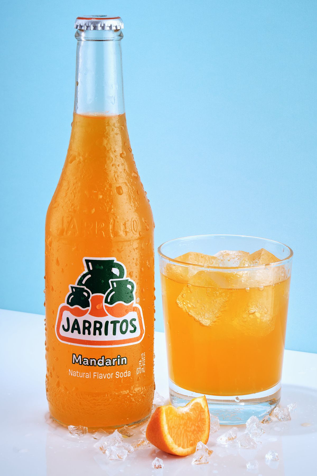 Bottle of Jarritos Mandarin soda beside a full glass and a tangerine slice.